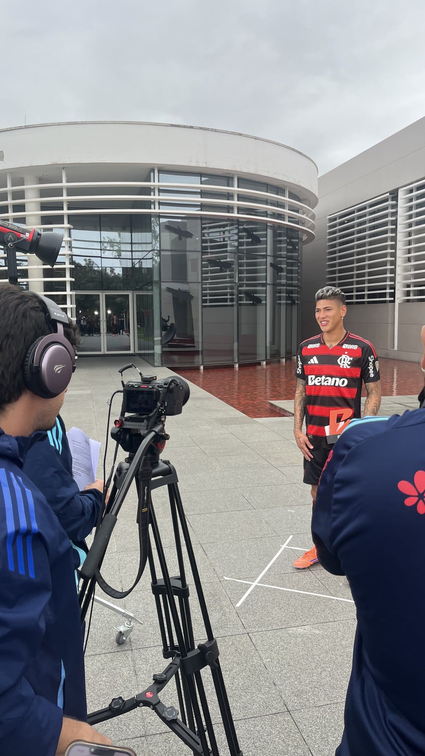 Câmera em tripé grava um jogador do Flamengo na frente do centro de treinamento