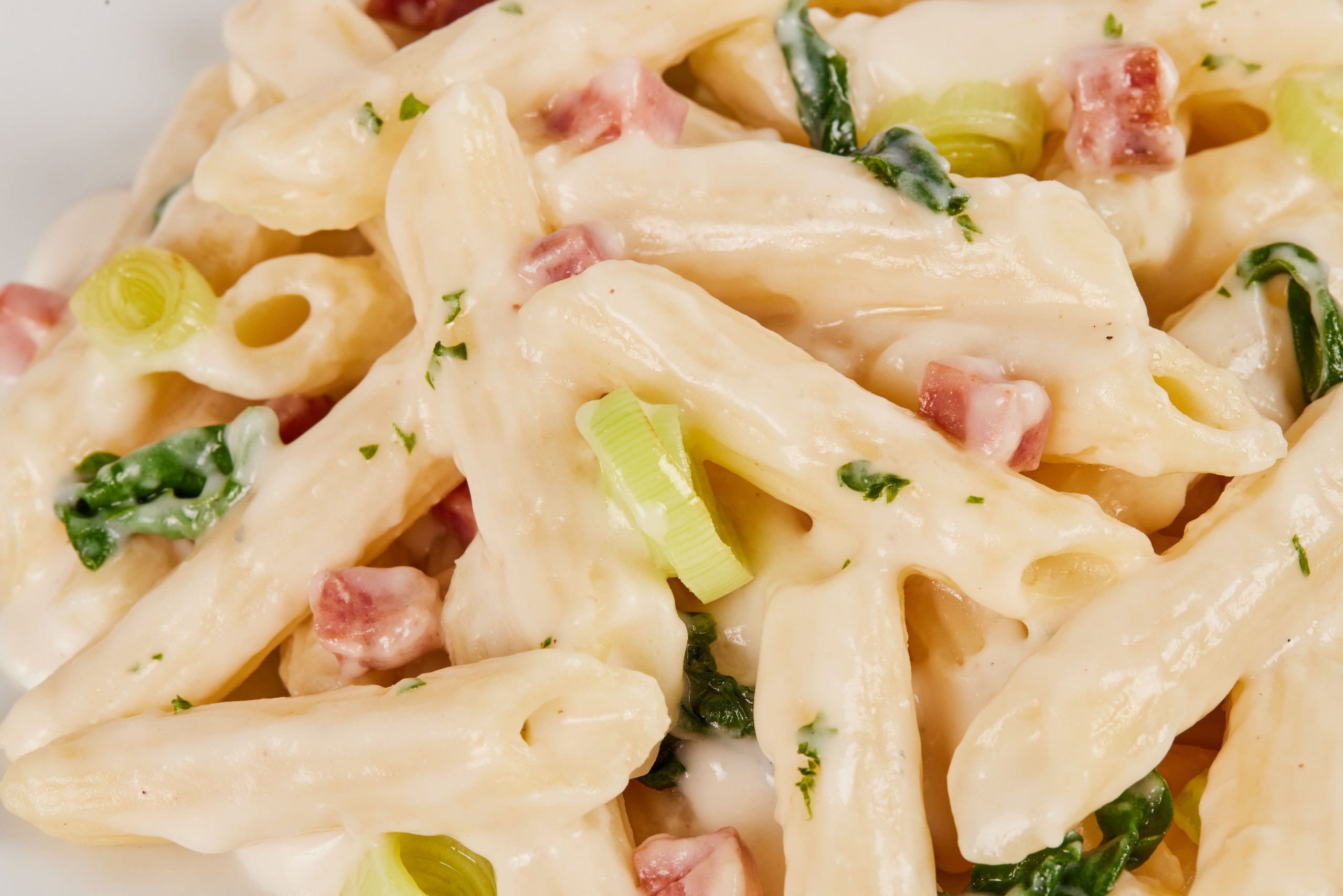 Detalhe do penne com molho branco, bacon e espinafre