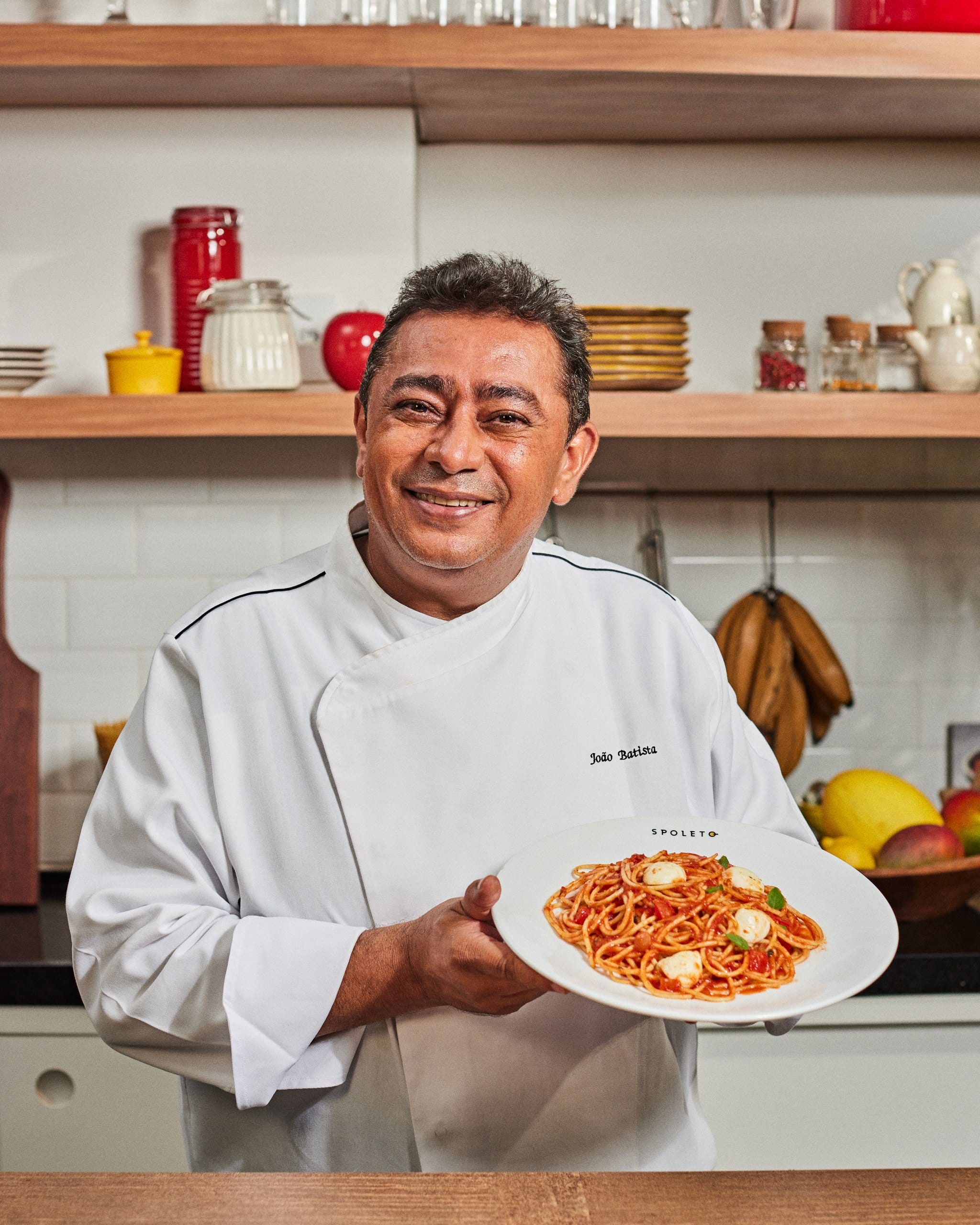 O chef João Batista segura um prato de espaguete com molho de tomate na cozinha