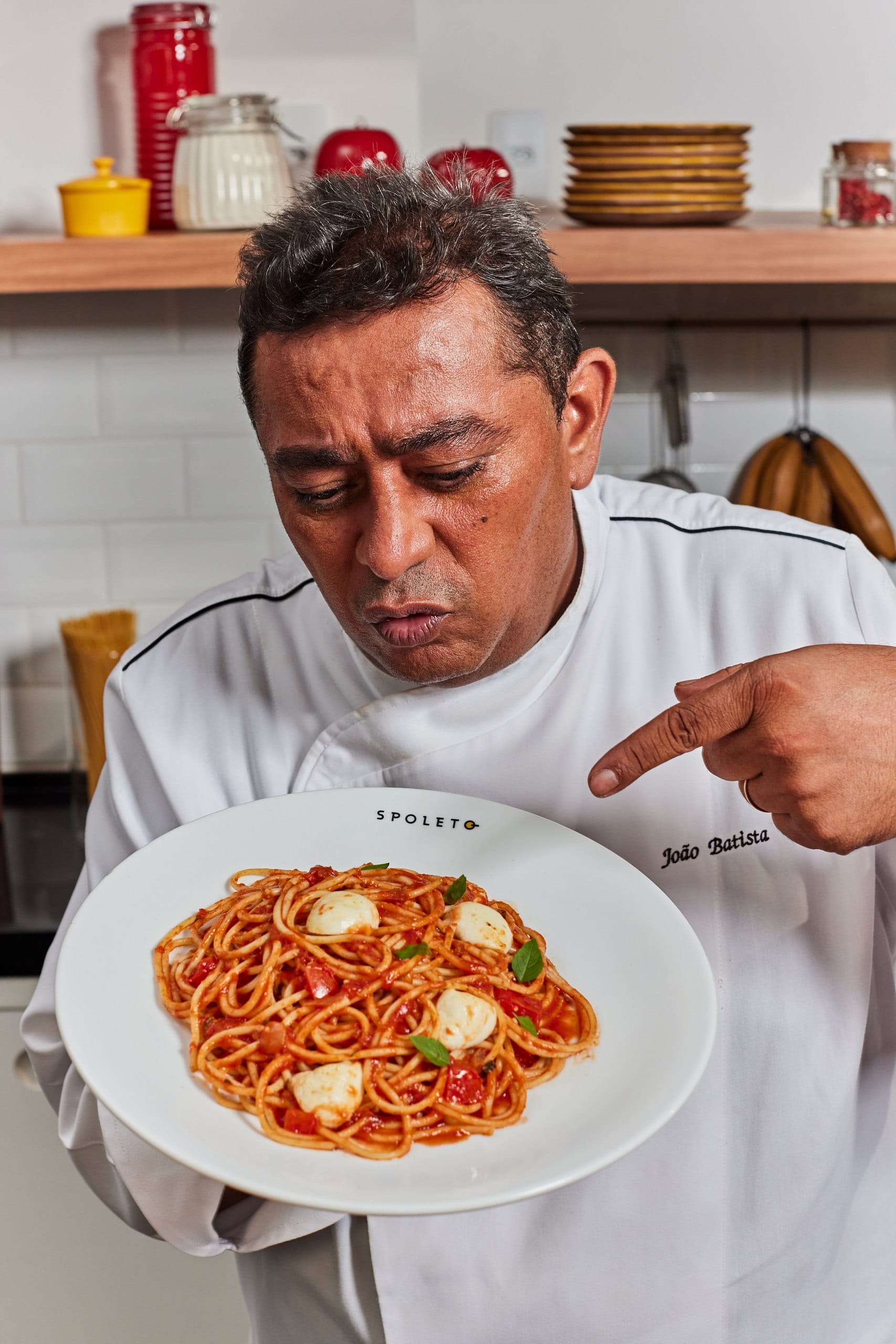 O chef João Batista olha para o prato de espaguete que segura