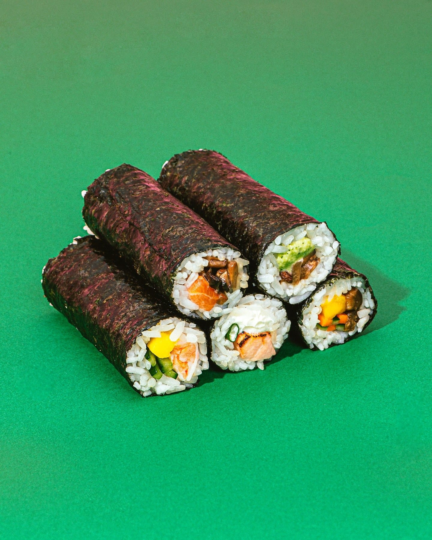 Três hand rolls empilhados sobre fundo verde