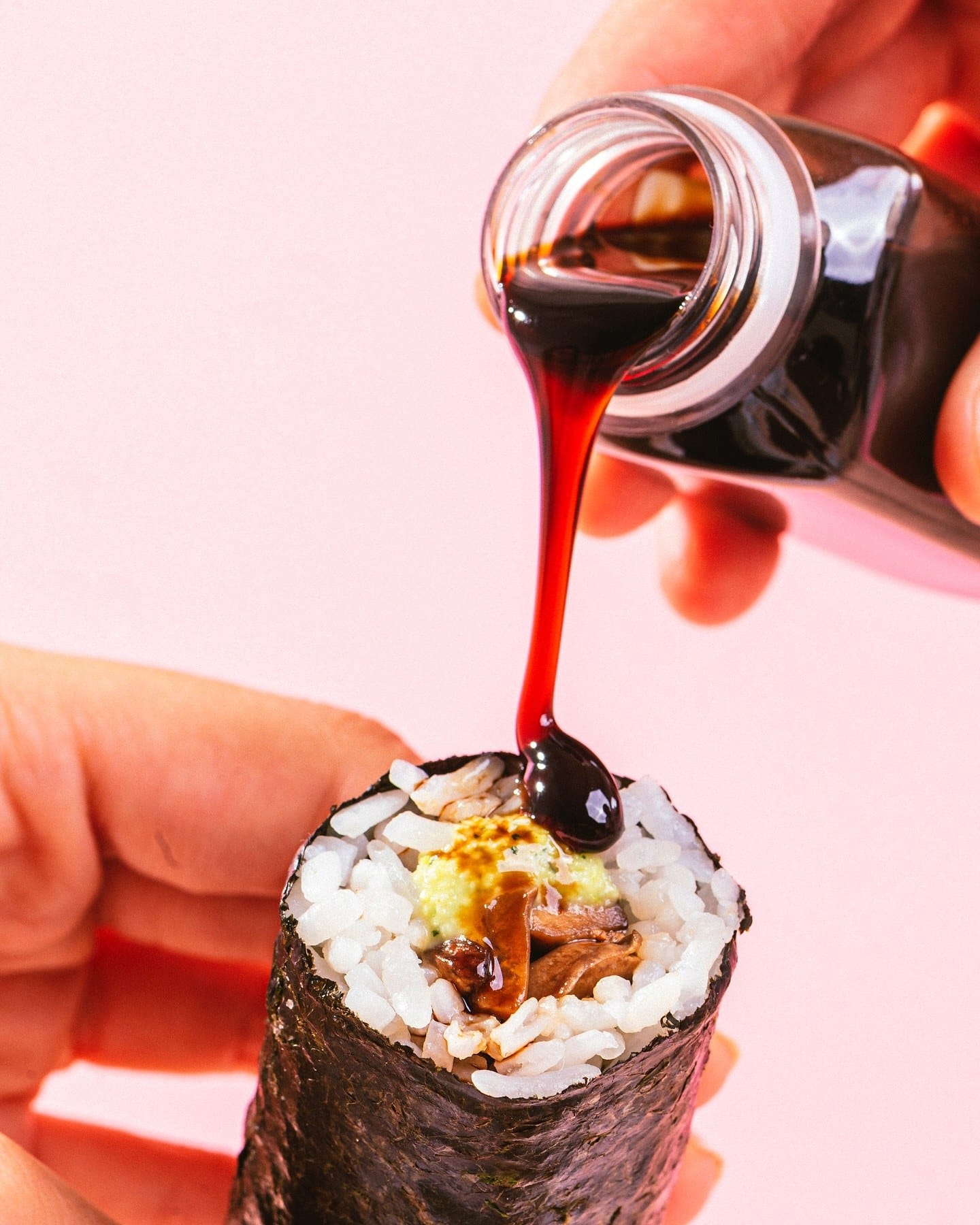 Shoyu sendo despejado sobre um hand roll, com fundo rosa